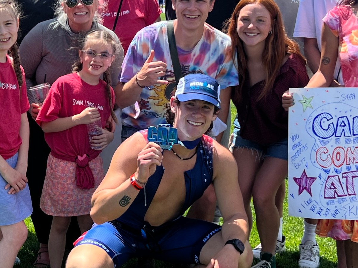Group photo of smiling people outside, one holding a medal and others holding signs.